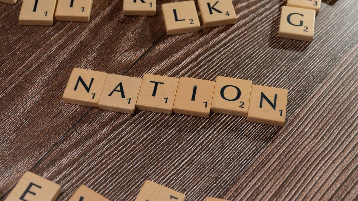 Close-up of wooden letter tiles spelling 'Nation' arranged on a brown wooden table surface.