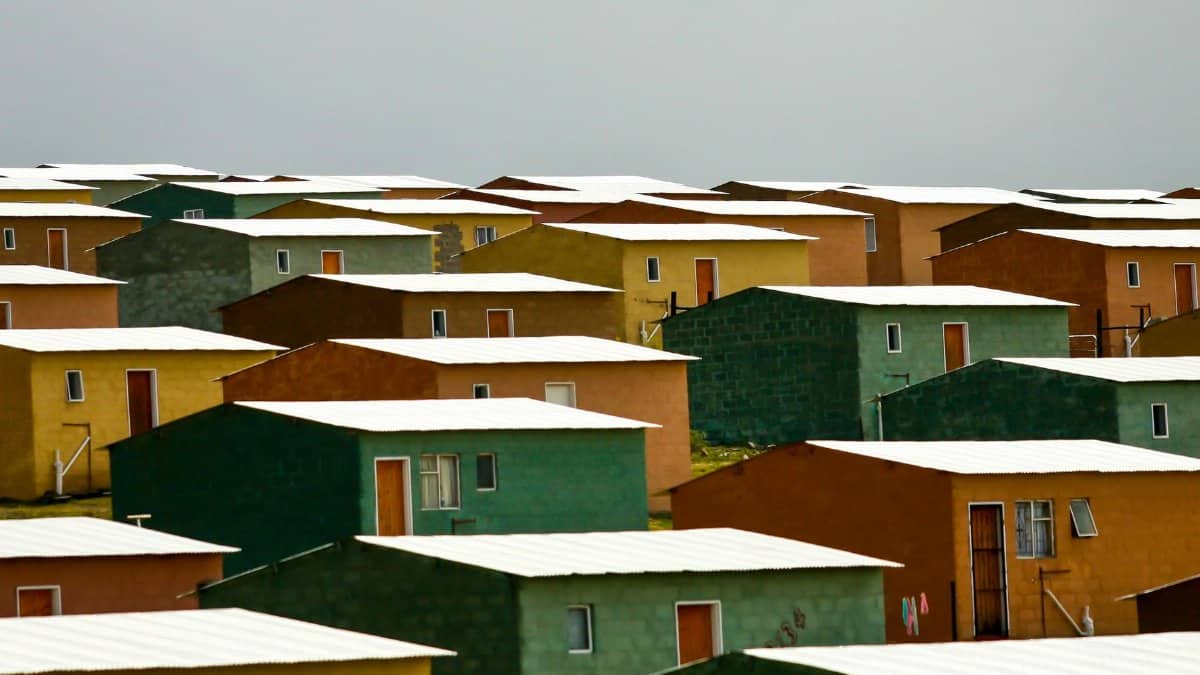 A vibrant cluster of colorful rectangular houses with white roofs in an urban setting under a cloudy sky.