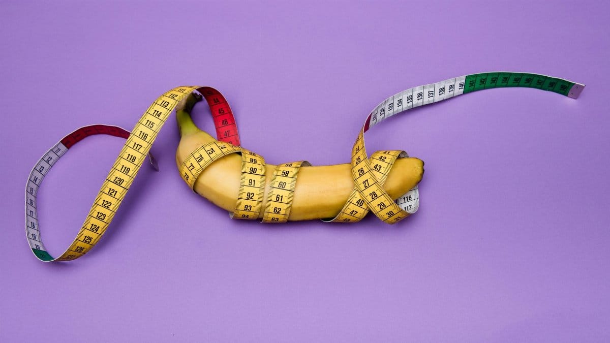 A banana wrapped in a measuring tape against a purple background, representing size and measurement concepts.