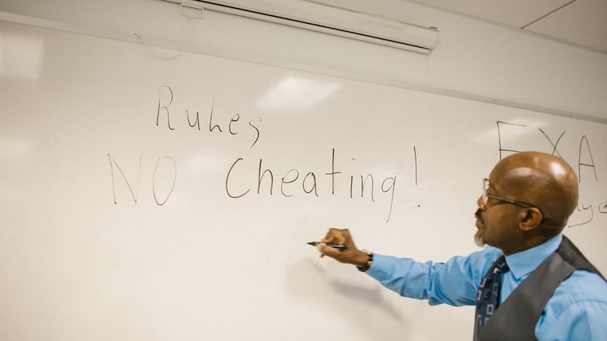 Teacher writes 'No Cheating!' on whiteboard during classroom instruction.