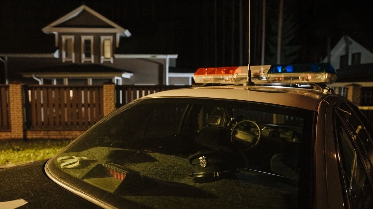 A parked police car at night in front of suburban houses with lights on, creating a dramatic mood.