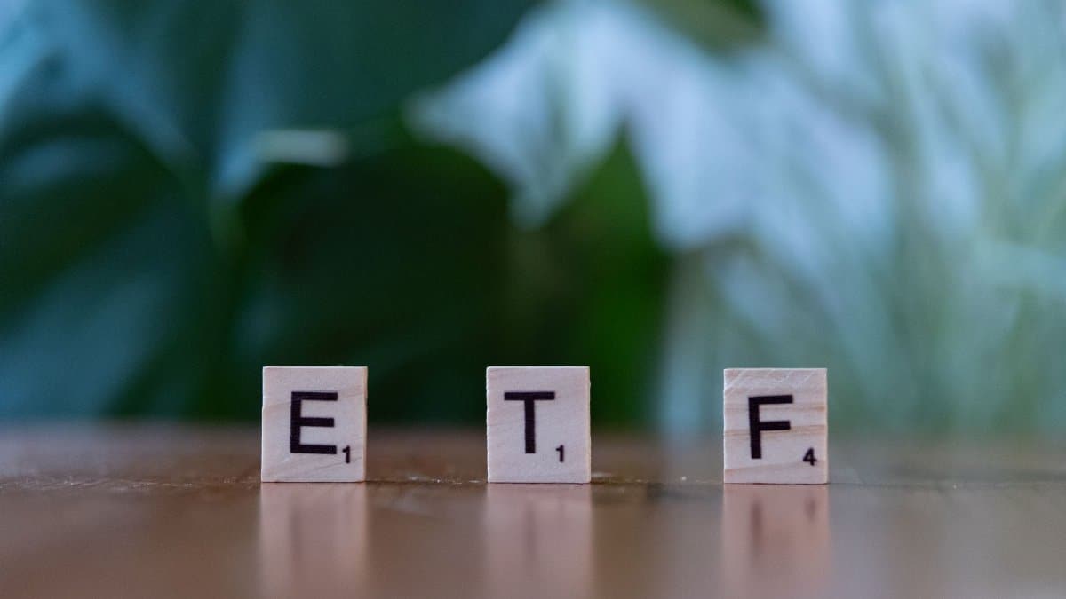 Scrabble tiles spelling ETF on a wooden surface with blurred green background.