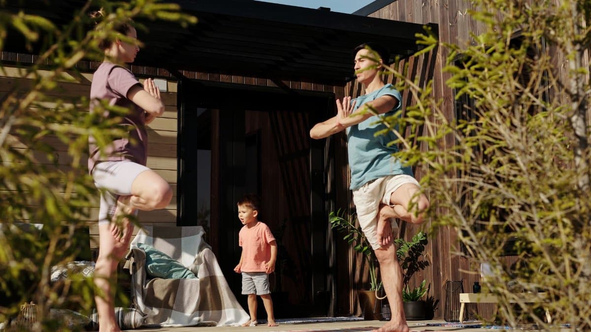 A family practicing yoga in tree pose on a sunlit porch, promoting health and mindfulness.
