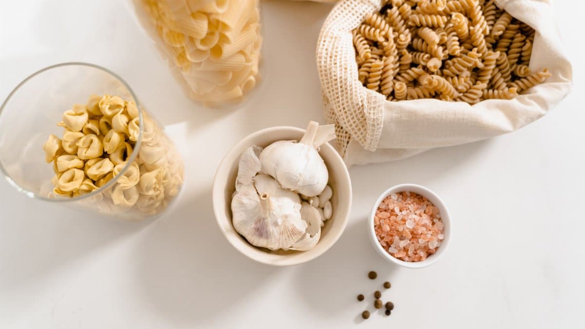 A top view of organic pasta ingredients and seasonings, featuring garlic, pink salt, and reusable bags.