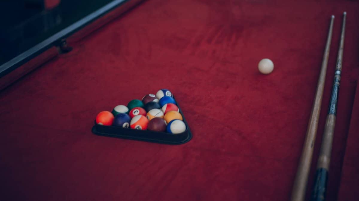 A classic billiard setup with a triangle of pool balls and cues on a red table.