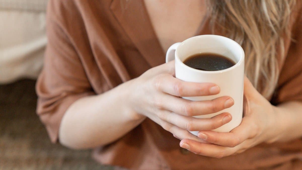 Close-up of a person holding a white mug filled with black coffee, showcasing a cozy and relaxed atmosphere.