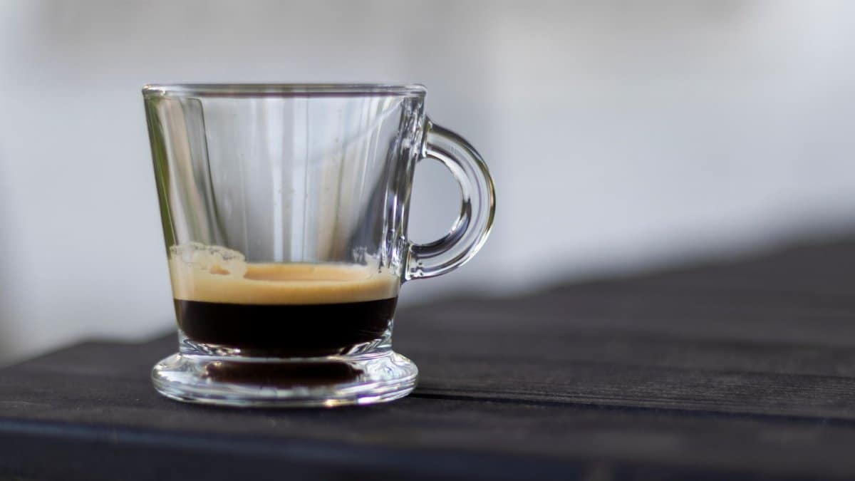 A close-up shot of a rich espresso in a clear glass cup on a dark table.