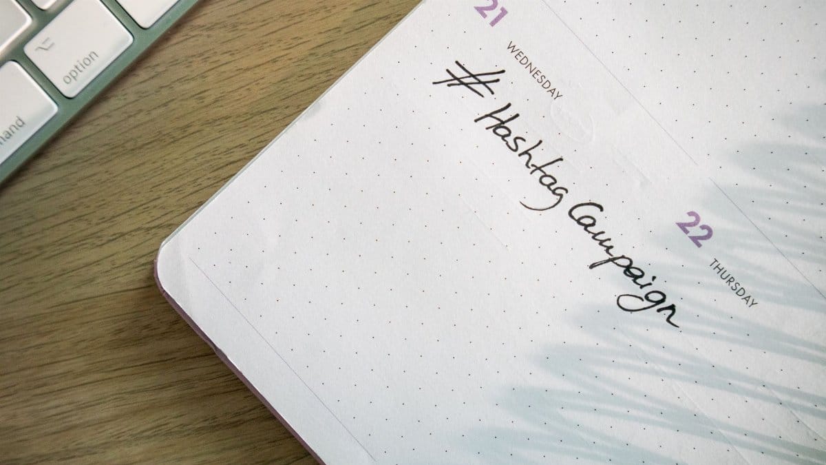 Open planner with 'Hashtag Campaign' handwritten next to keyboard. Ideal for social media and productivity themes.