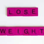 Creative image of the phrase 'Lose Weight' spelled with Scrabble tiles on a white background.
