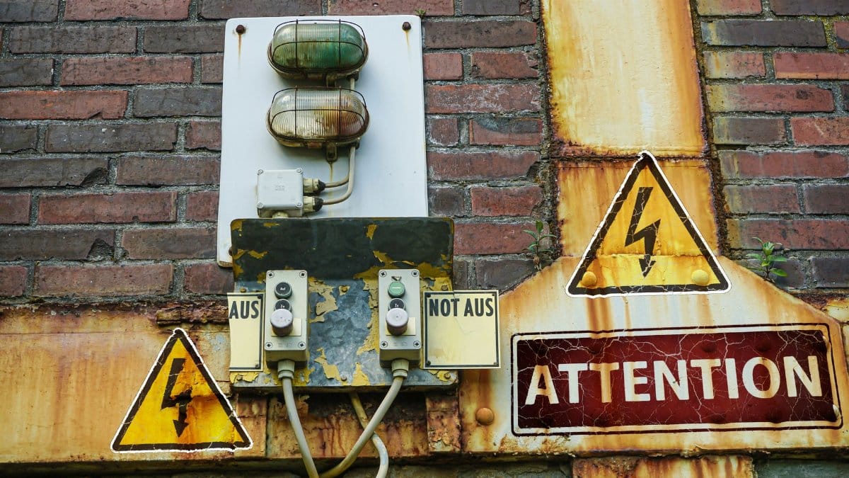 A close-up of an old, rusty warning sign and electrical components on a brick wall conveying caution.