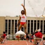 Male athlete performing a long jump at a track event in Houston, TX, showcasing athleticism and determination.