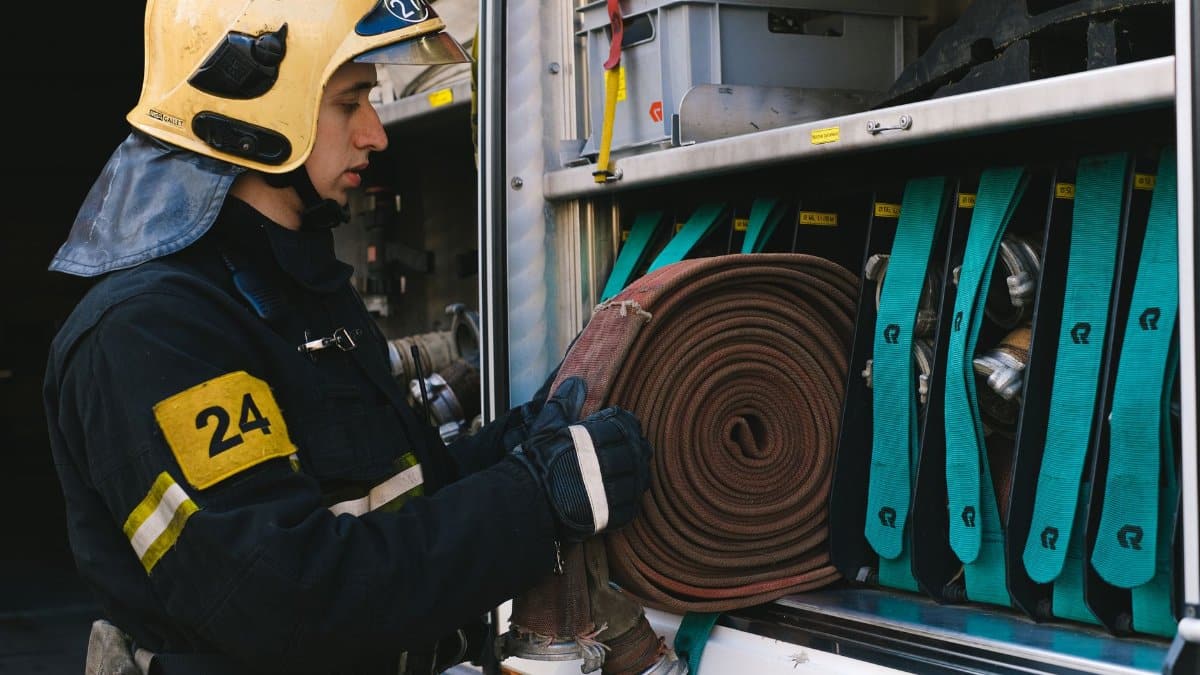 Firefighter organizing hoses in a fire truck, focusing on readiness and safety.