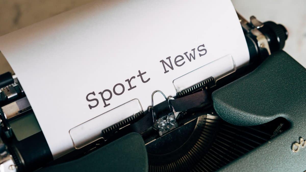 Close-up of a vintage typewriter with 'Sport News' typed on paper, evoking retro charm.