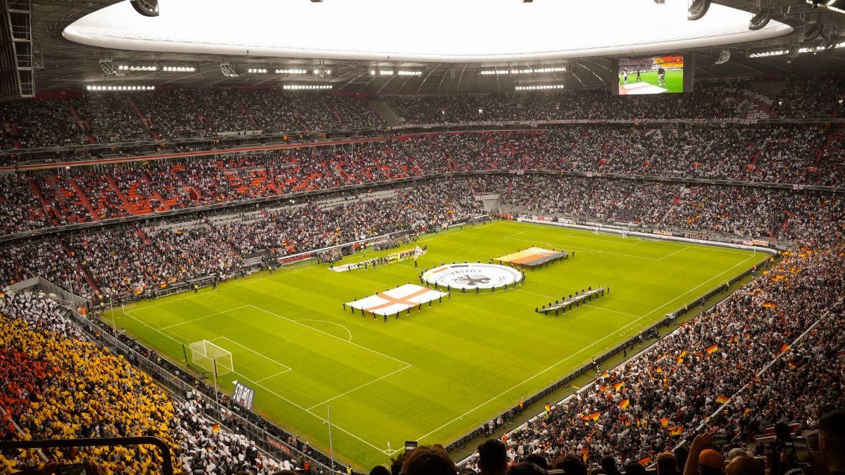 A packed stadium with fans watching a live soccer game, featuring vibrant crowd colors.