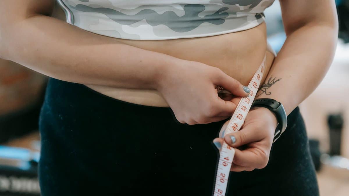 Crop anonymous plus size female with measuring tape measuring waist on blurred background