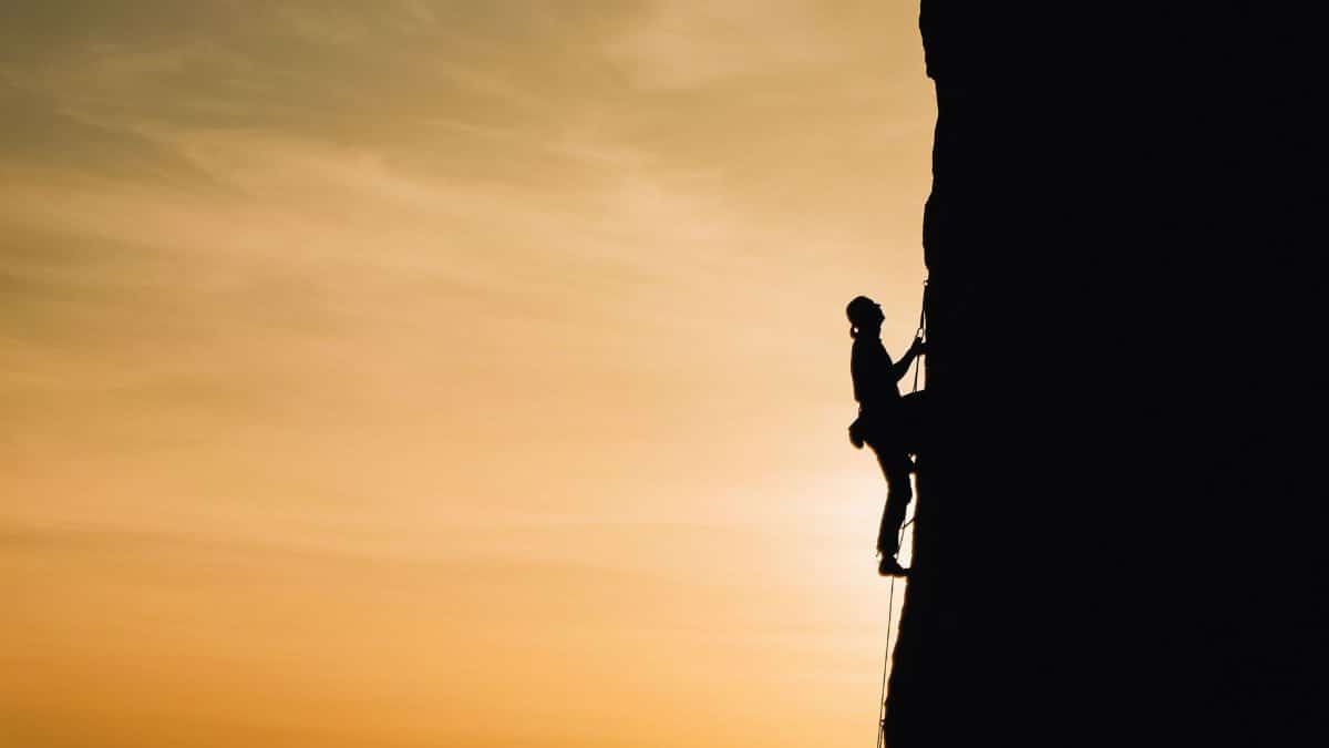 A silhouette of a rock climber scaling a steep cliff during sunset in Russia, showcasing determination and adventure.