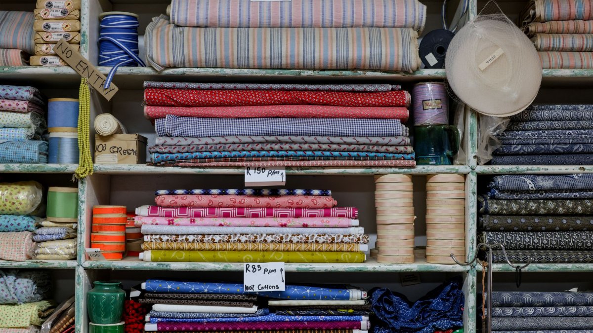Organized shelves with various colorful fabrics, threads, and prices in a textile shop.