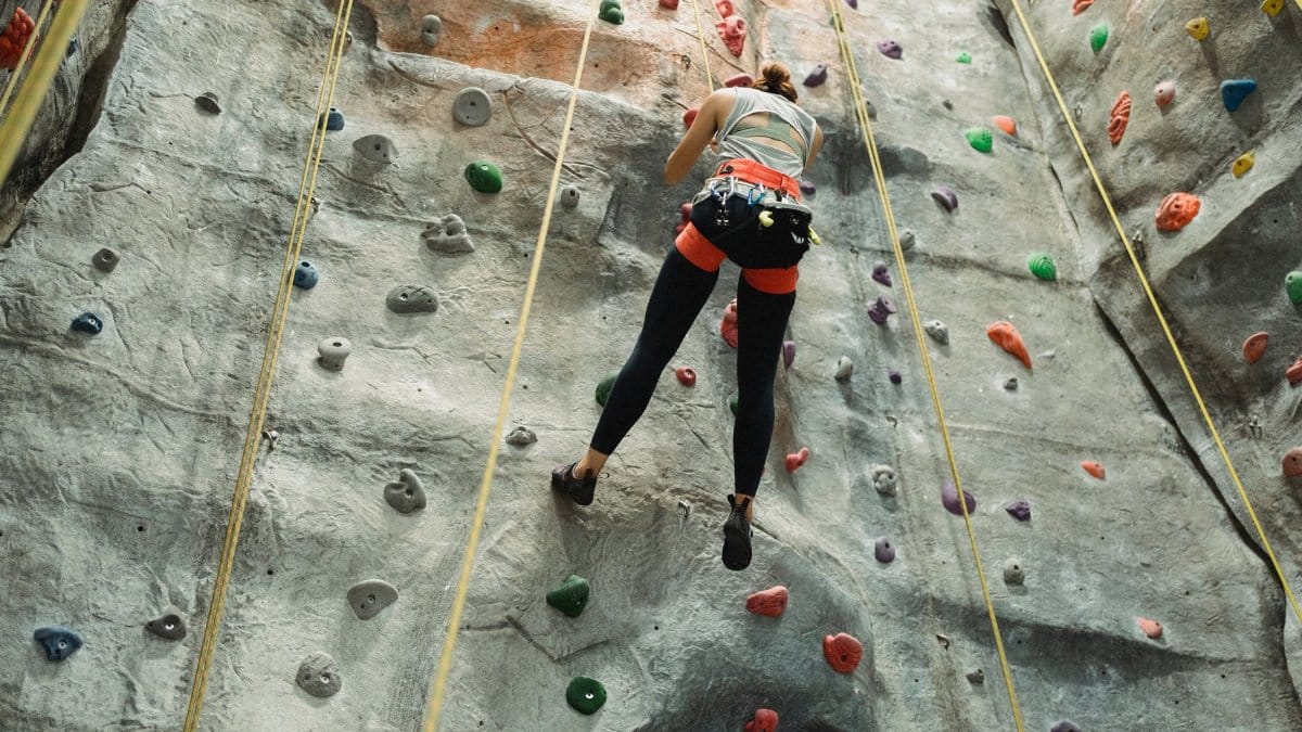 From below of unrecognizable female climbing and hanging with rope on gray boulder