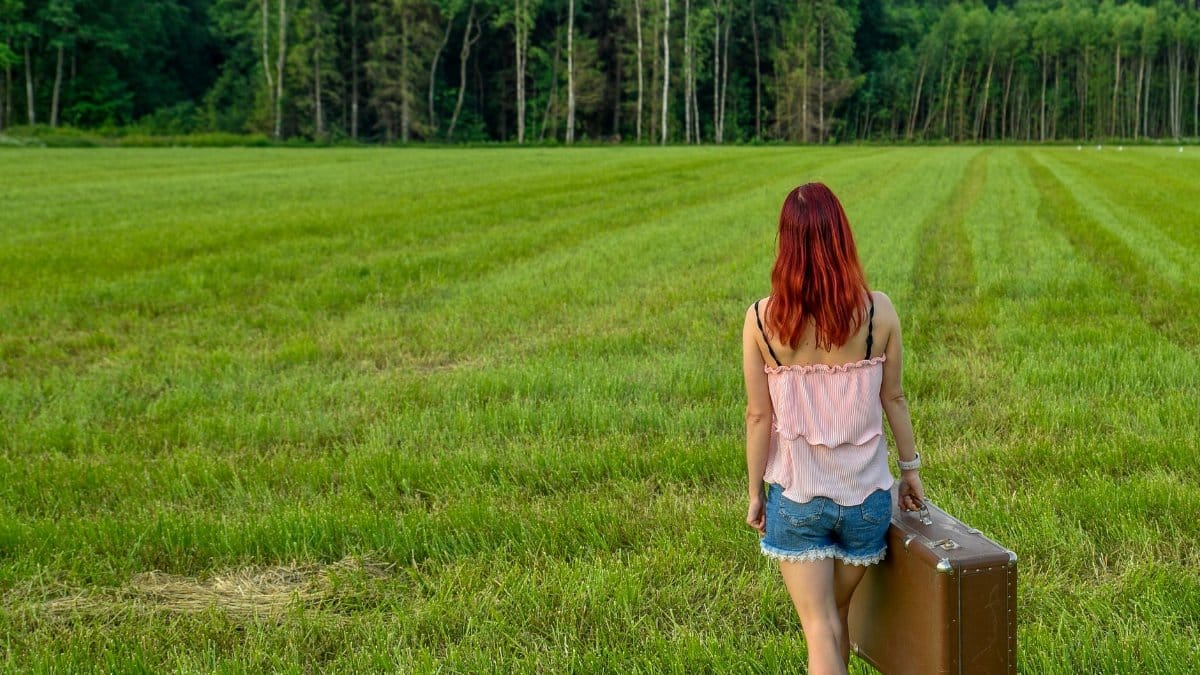 Woman with suitcase walking through grassy fields in Kolga, Estonia, representing freedom and adventure.