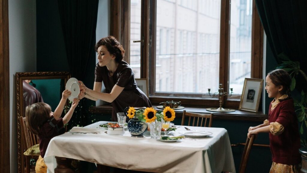 A mother and children engage in a fun meal scene with sunflowers on the table.