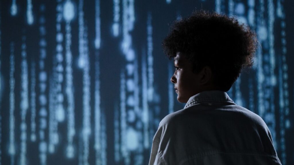 Side view of a teenager observing futuristic digital code on a screen.