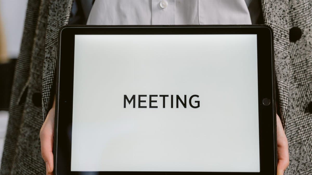 Close-up of a tablet with 'MEETING' on the screen held by a person in a blazer.