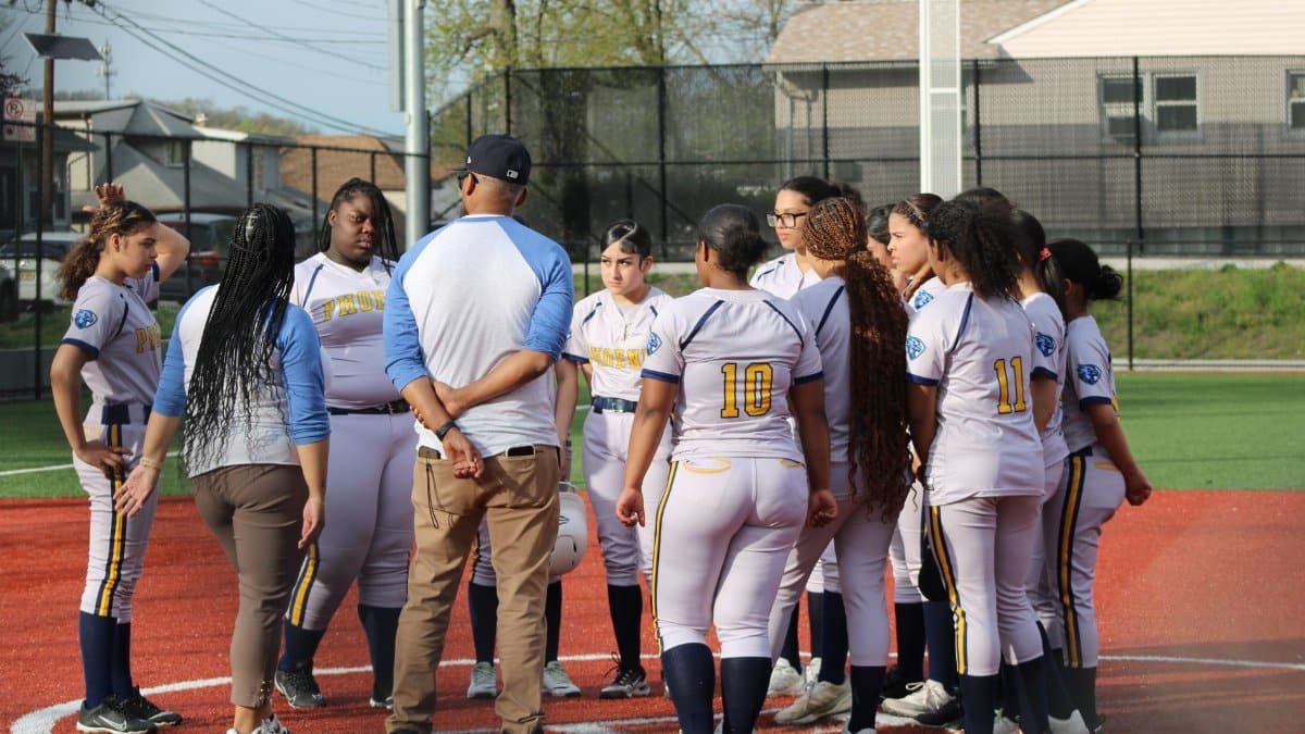 A girls' softball team gathers around their coach on the field for a strategic discussion.