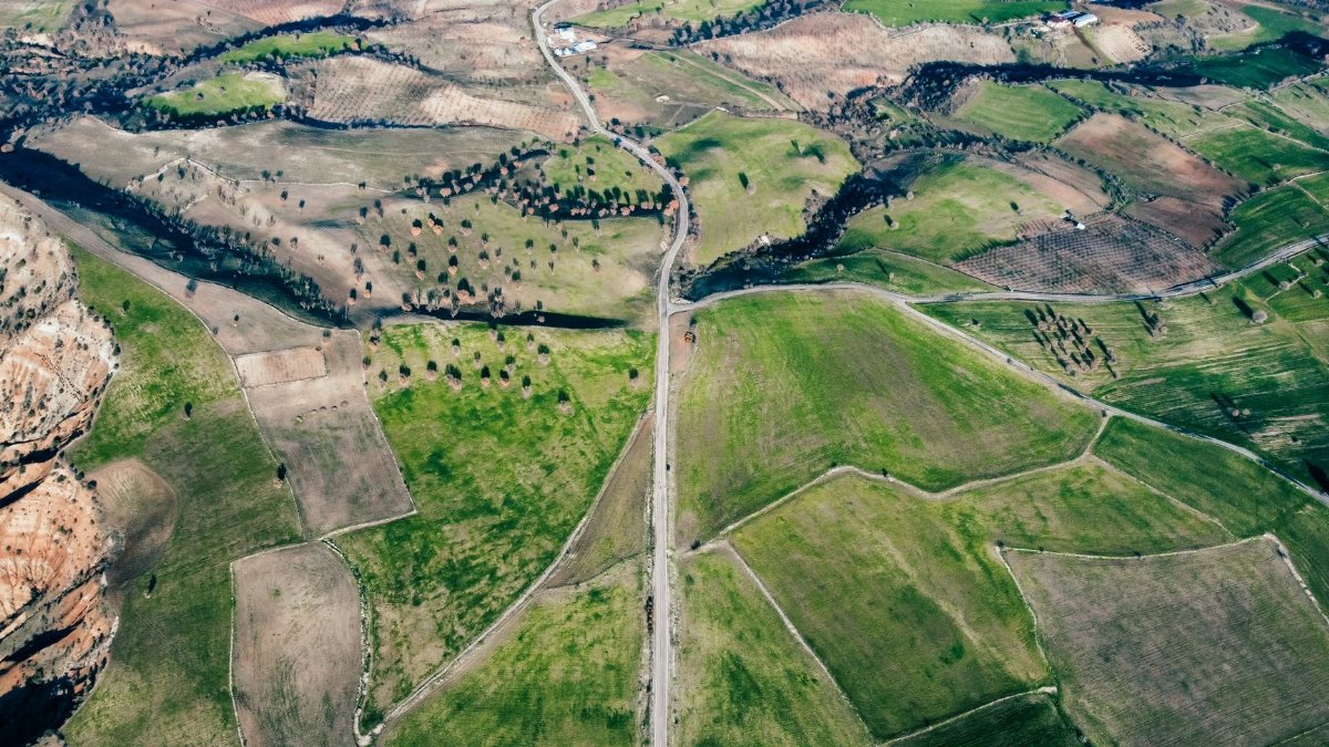 Stunning aerial view of expansive green fields and winding countryside road under a clear sky.