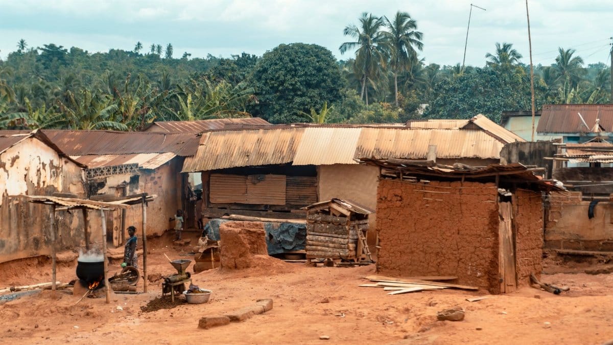 A rustic village scene depicting clay and corrugated iron huts, outdoor cooking, and daily life.
