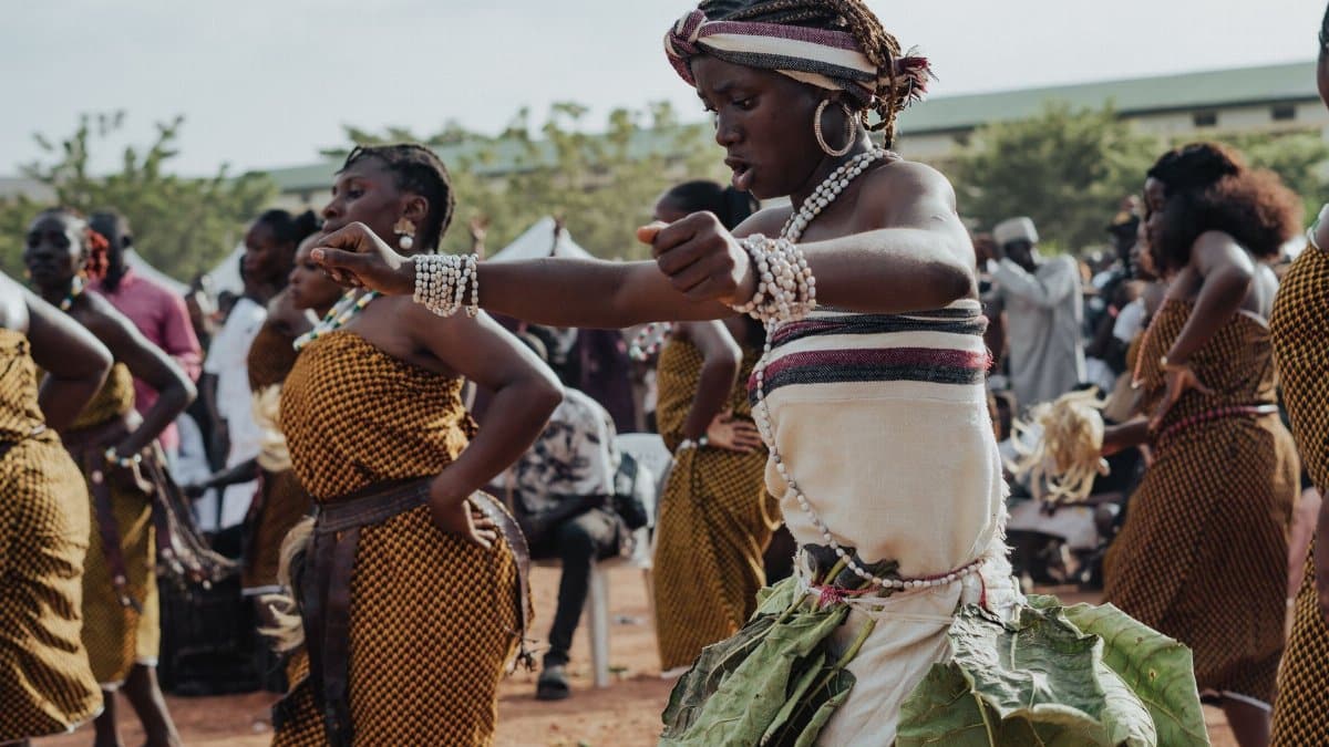 African women performing a vibrant traditional dance outdoors, showcasing cultural attire and expressions.