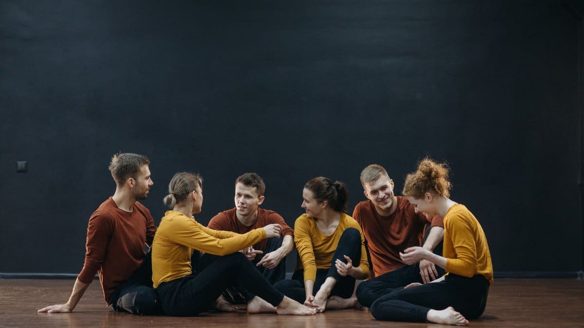 Casual group of adults relaxing in a dance studio with wooden floors and dark walls.