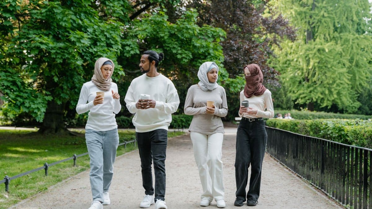 Group of young adults walking together with coffee in a scenic park setting during the day.