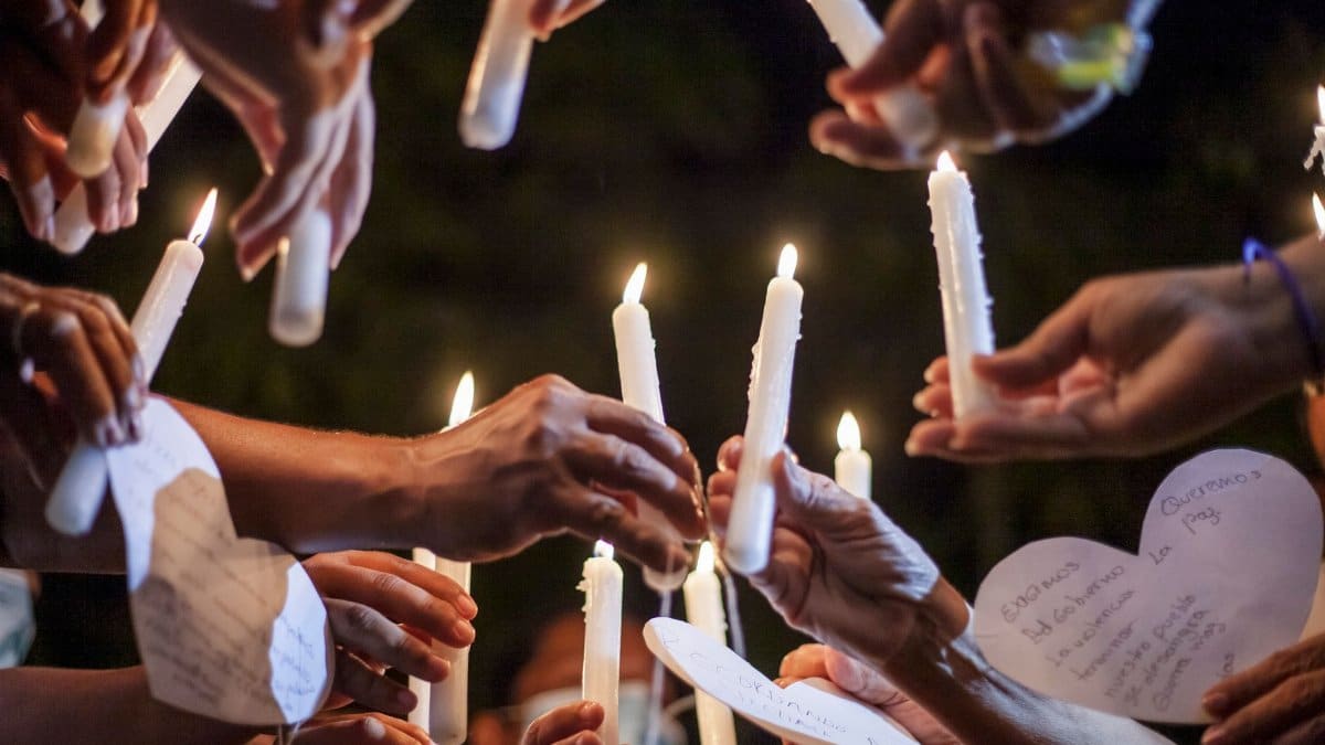 Candlelight vigil with hands holding candles and heart-shaped messages at night in Ovejas, Colombia.