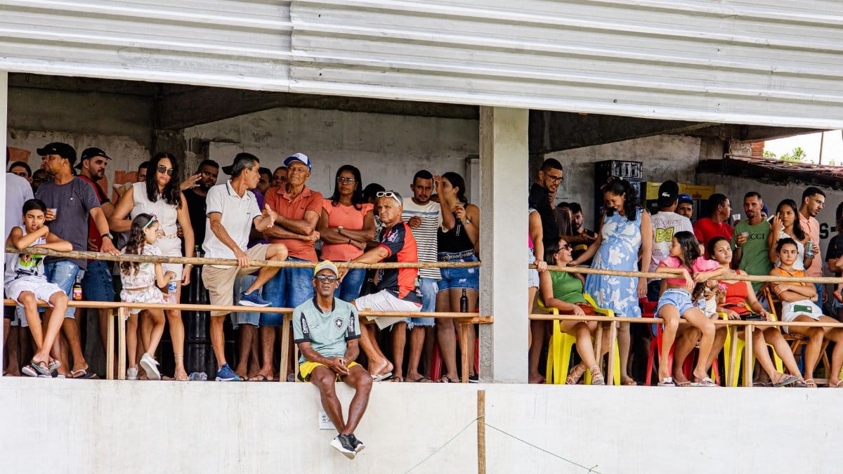A diverse group of people gathered on a balcony, watching an outdoor community event in the daytime.