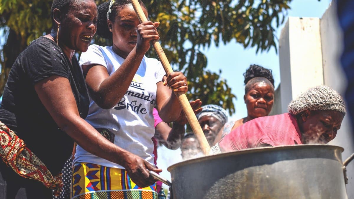 A group of women collaborating to stir a huge pot of food outdoors. Vibrant and community-focused.