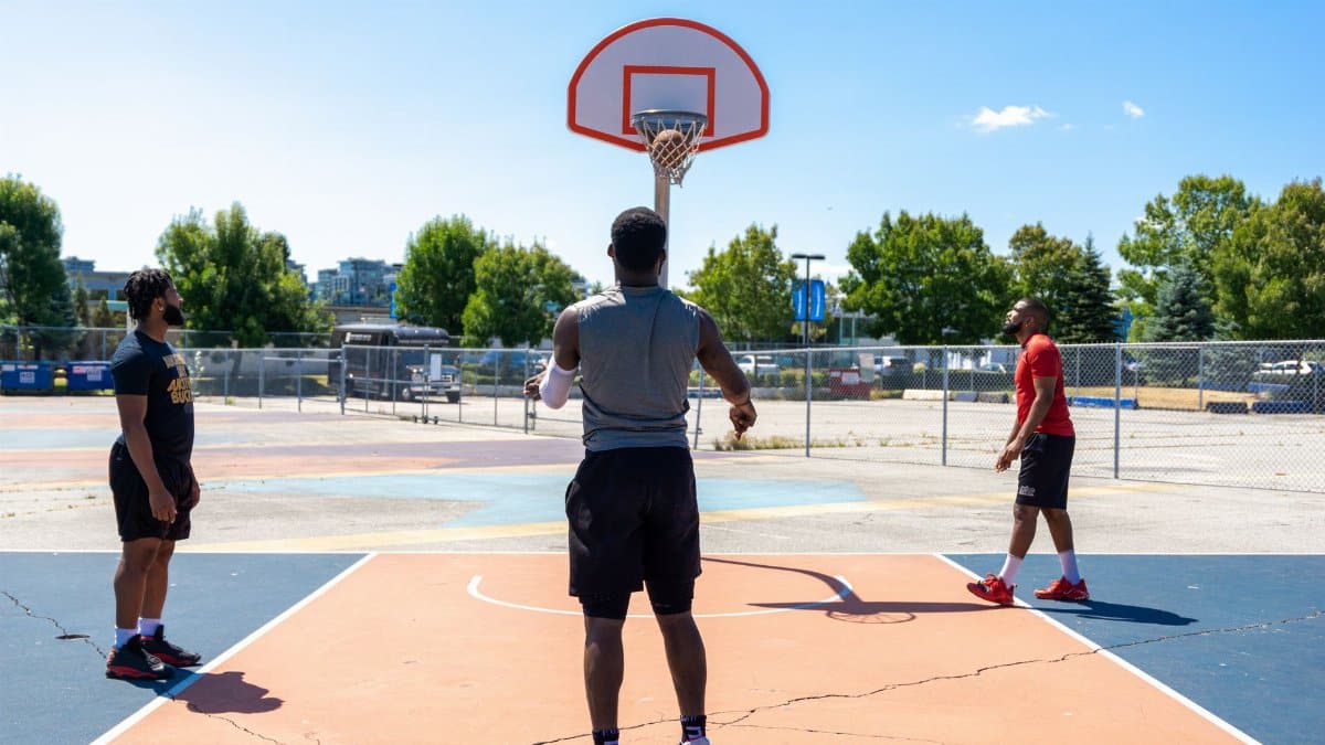 Three men playing basketball on an outdoor court on a sunny day.