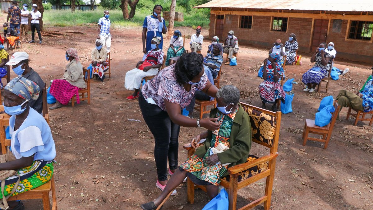 High angle of anonymous African female taking care of senior people in face masks sitting on chair near shabby building of nursing home in village