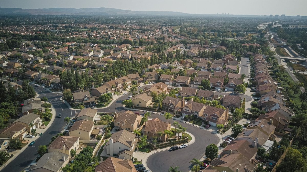 Drone shot capturing a sprawling residential area with homes, roads, and trees.