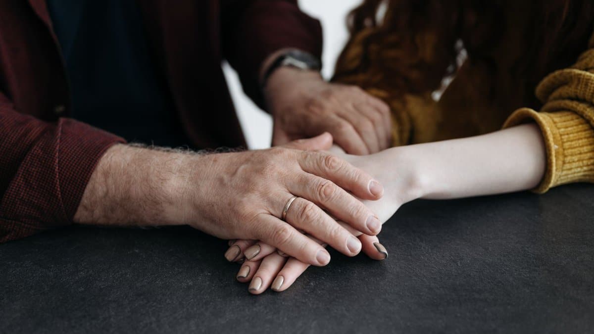 Close-up image of people holding hands, illustrating support and connection indoors.