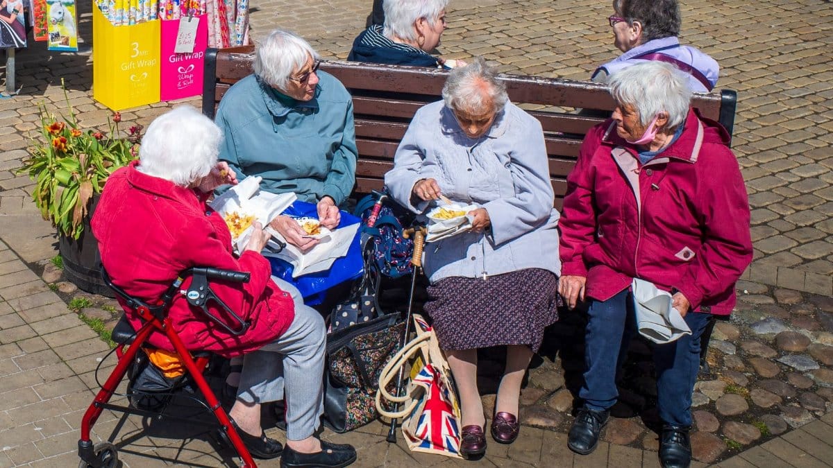 Group of elderly women sharing a meal on a sunny day in Liverpool, UK, showcasing friendship and community.