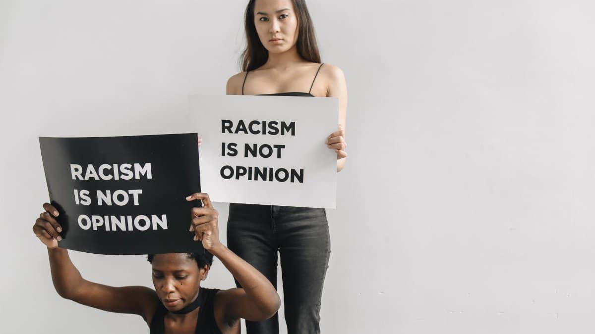 Two women holding placards with 'Racism is Not Opinion' message, promoting equality.