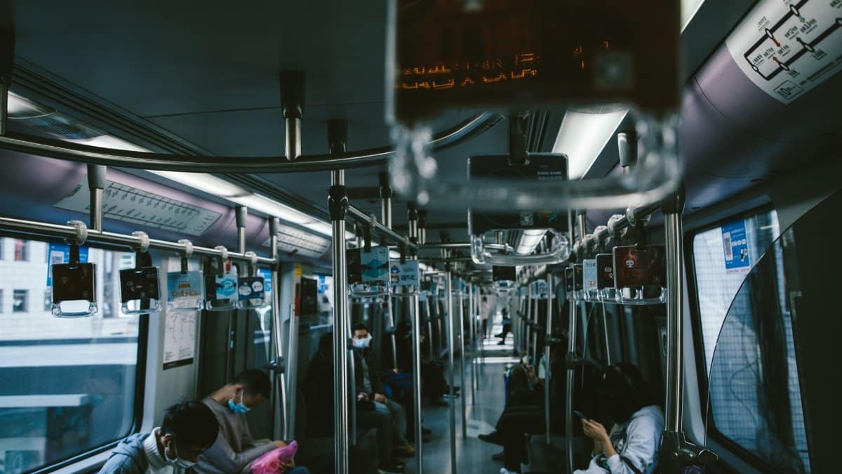 A calm scene of masked commuters sitting inside a modern subway train, maintaining social distance.