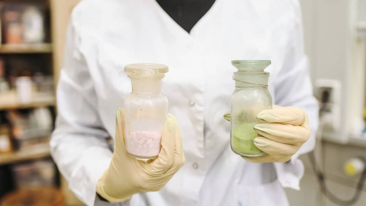 A lab technician holds two chemical bottles in a laboratory setting, wearing gloves and a lab coat.