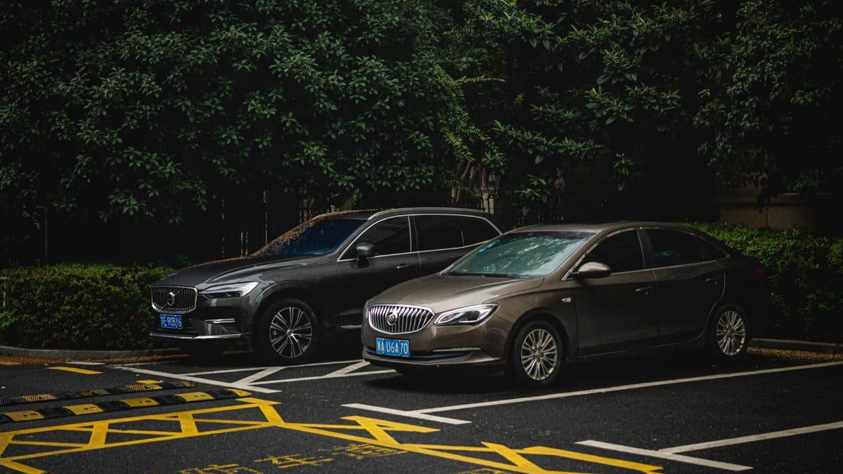 Two cars, an SUV and a sedan, parked side by side in a shady urban lot.