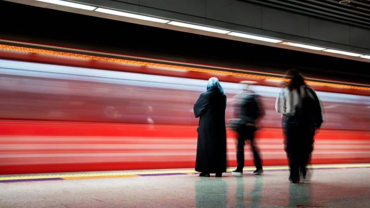 Underground station with a passing blurred red train and waiting passengers.
