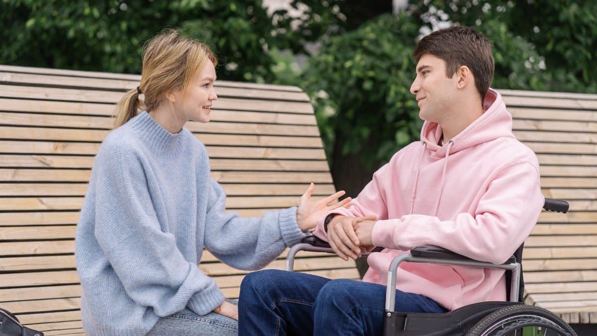 Young adults engaging in a warm conversation outdoors, one in a wheelchair.