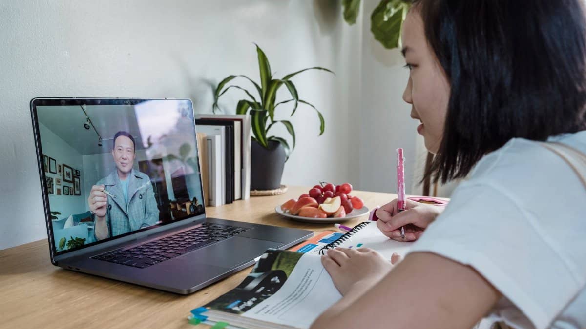 Young girl engaged in online learning via video call, studying with laptop and notes.