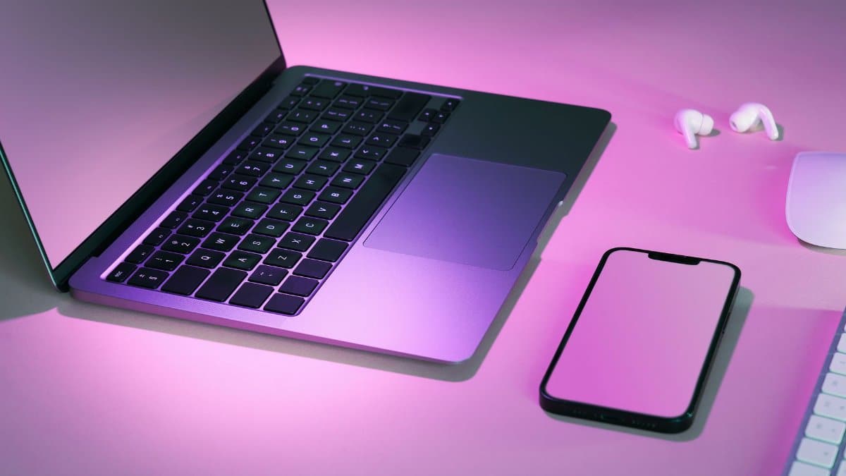 Stylish tech workspace featuring a laptop, smartphone, and earphones under pink lighting.