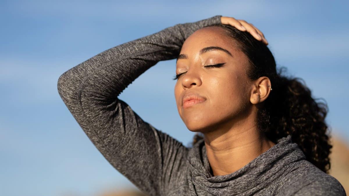Close-up portrait of a woman enjoying sunlight with eyes closed, wearing a gray long sleeve shirt.