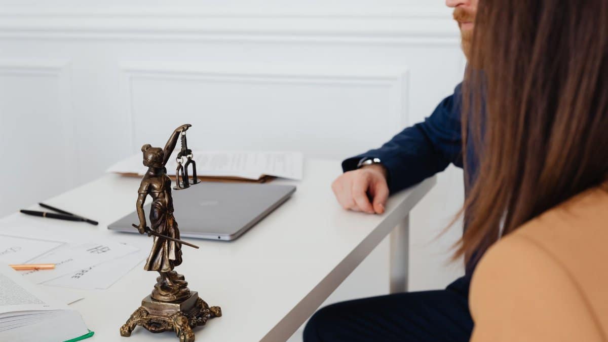 Professional setting with lawyers and Lady Justice statue discussing legal documents.